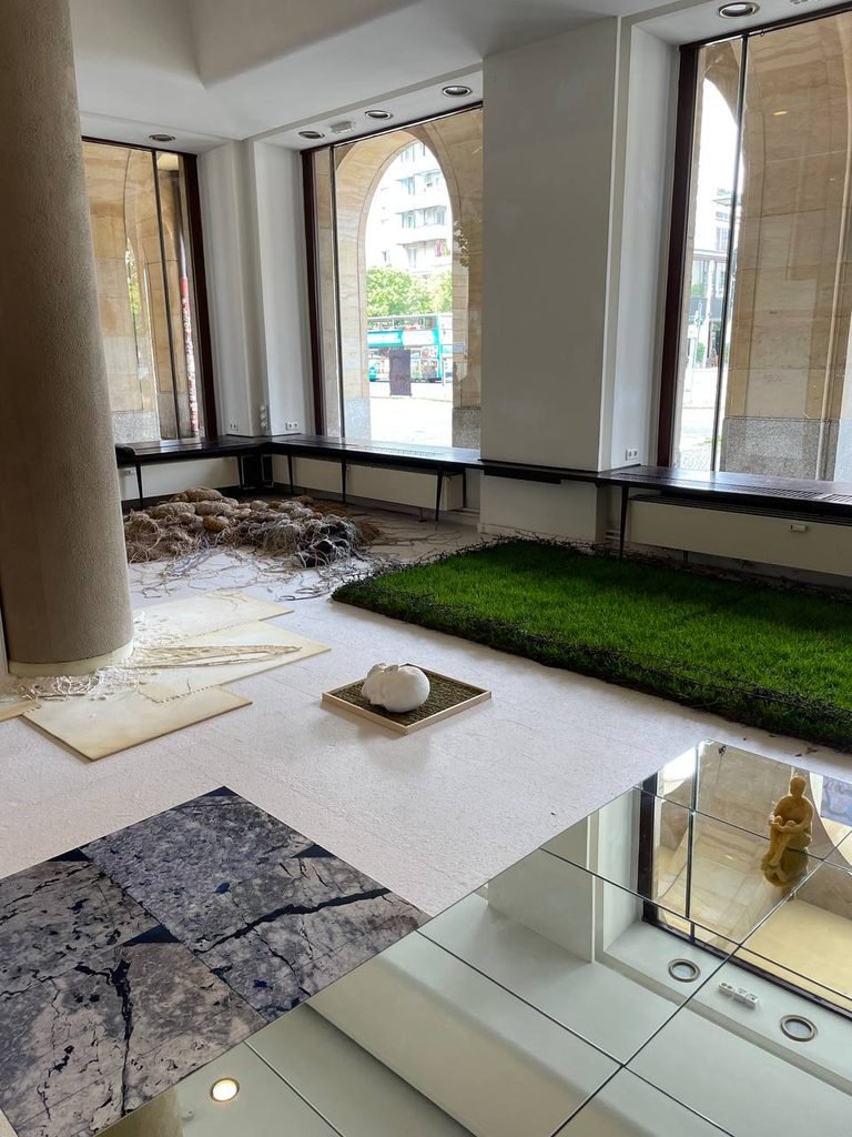 Wide view of the exhibition space with walkable mirrors installed across the floor and small sculptural figures placed on the reflective surface.