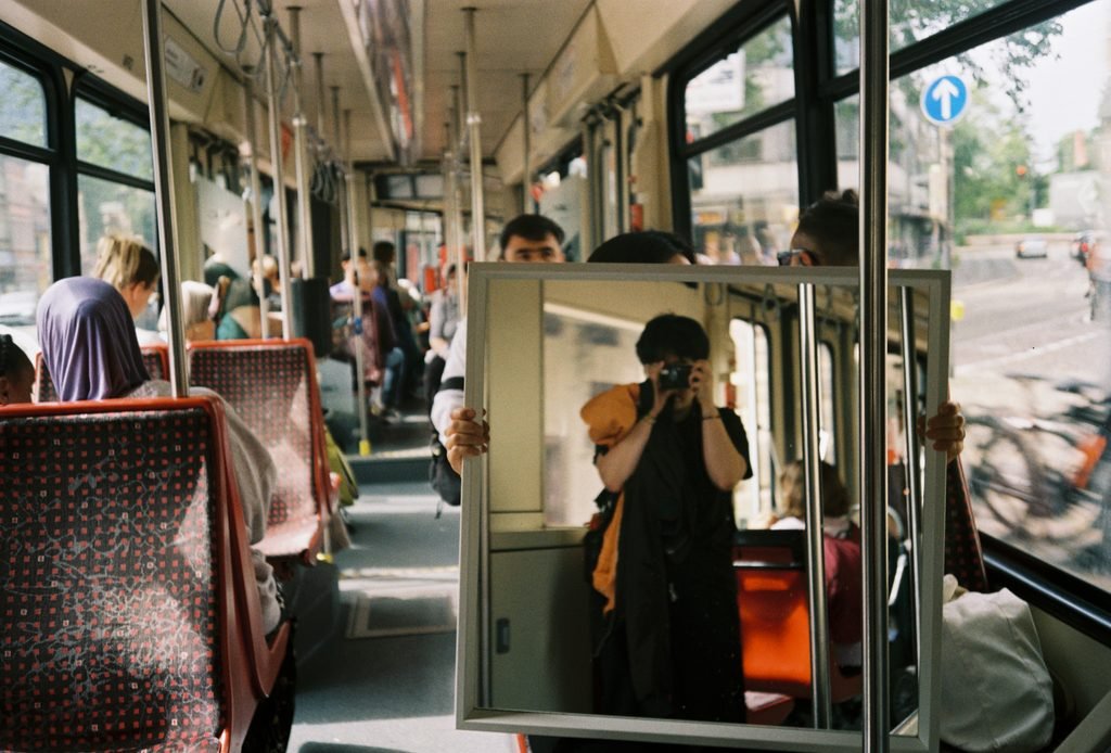 Large mirror inside a tram reflecting the photographer and the interior of the vehicle.