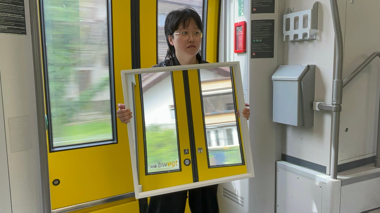 Performer holding a large mirror in front of yellow doors inside a moving tram in Freiburg.