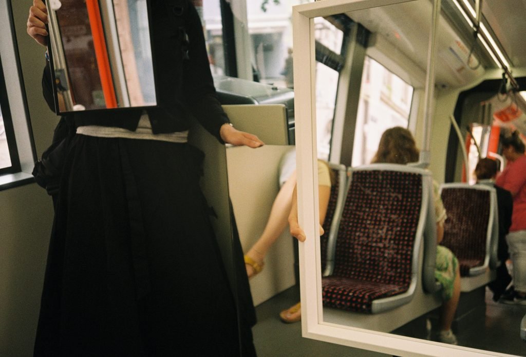 Two mirrors inside a tram overlapping and connecting seats, passengers, and window surfaces.