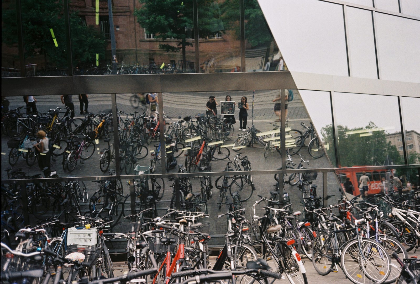 Reflective glass façade in Freiburg with bicycles, pedestrians, and multiple overlapping reflections.