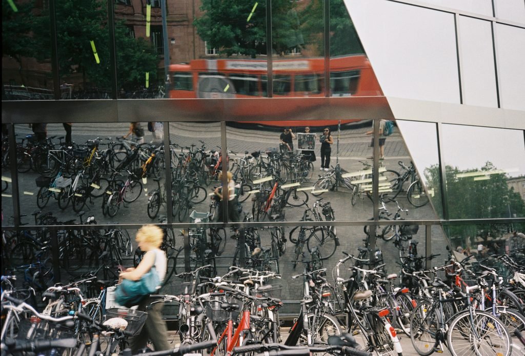Reflective glass façade in Freiburg showing bicycles, pedestrians, and a passing red tram.